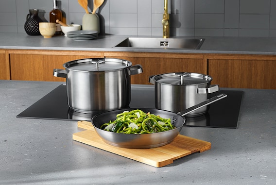 Een keuken met een eiland waarin een ingebouwde AEG inductiekookplaat ligt waar pannen op staan en ernaast een snijplank ligt met een koekenpan met voedsel erin